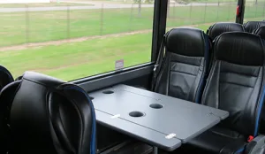 Interior of a charter bus featuring black leather seats and a center table with cup holders