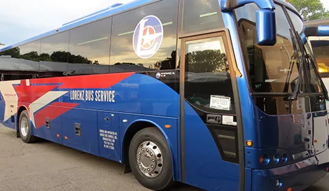 Lorenz Bus Service motorcoach with blue and red livery parked at a transportation staging area