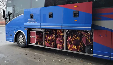 Undercarriage storage compartments of a charter bus packed with maroon and gold athletic gear bags