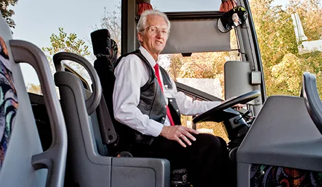 Professional bus driver in vest and tie seated at the wheel of a charter coach, ready to depart