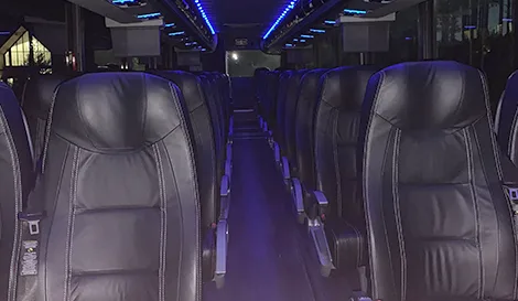 Interior of a charter bus with rows of black leather seats and blue ambient lighting