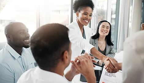 Two professionals shaking hands across a conference table while smiling colleagues look on during a business meeting
