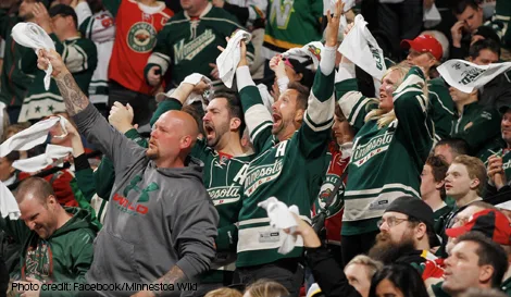 Minnesota Wild fans cheering in the stands, waving rally towels and wearing team jerseys