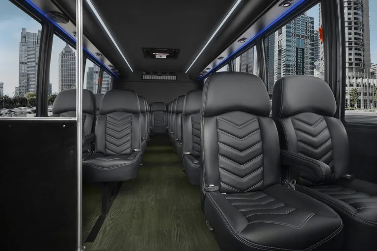 Interior of a charter bus with rows of black leather seats, wood-grain flooring, and LED lighting along the ceiling