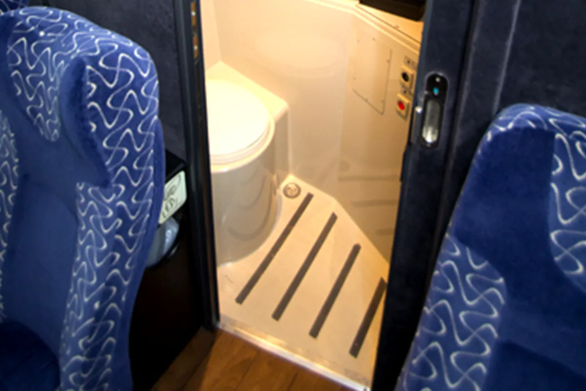 Onboard restroom with toilet and non-slip floor strips, viewed from the passenger cabin aisle between blue seats