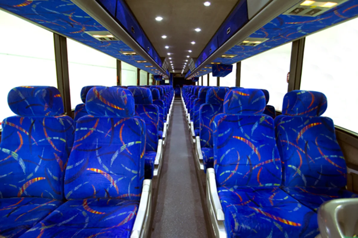 Interior of a full-size motorcoach with rows of blue patterned seats, a center aisle, and overhead lighting