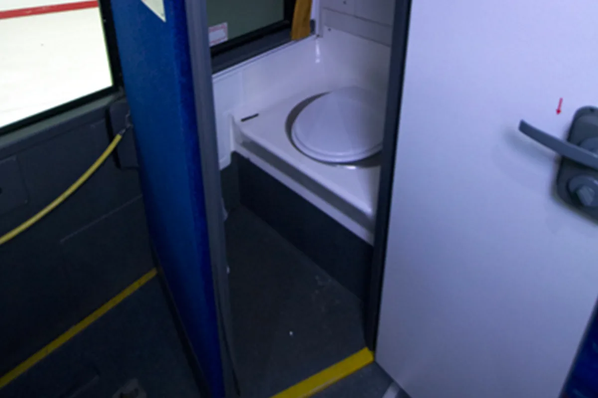 Onboard bus restroom with toilet and door, viewed from the aisle