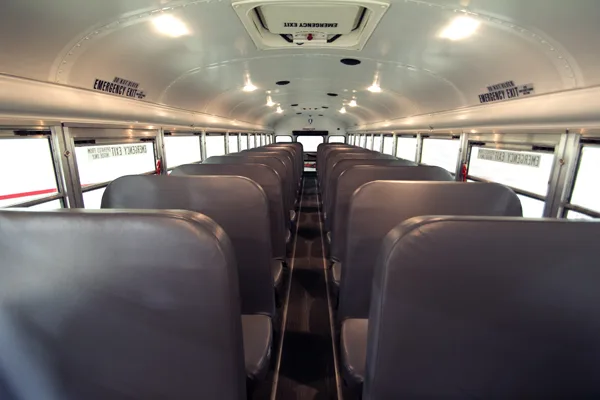 Interior view of a clean, full-size school bus with rows of gray seats, overhead lighting, and emergency exit signs