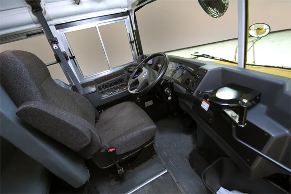 Interior view of a bus driver's cockpit showing the steering wheel, dashboard controls, and padded driver's seat