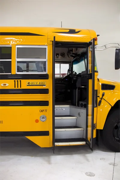 Blue Bird school bus number 111 with door open, parked in a garage facility
