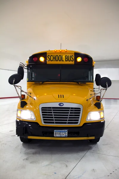 Yellow school bus number 111 with headlights on, photographed head-on inside a maintenance facility