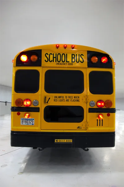 Rear view of a yellow Blue Bird school bus with flashing amber and red safety lights activated