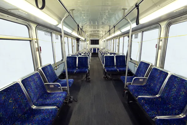 Interior of an empty bus with rows of blue patterned seats, grab bars, and large windows along both sides
