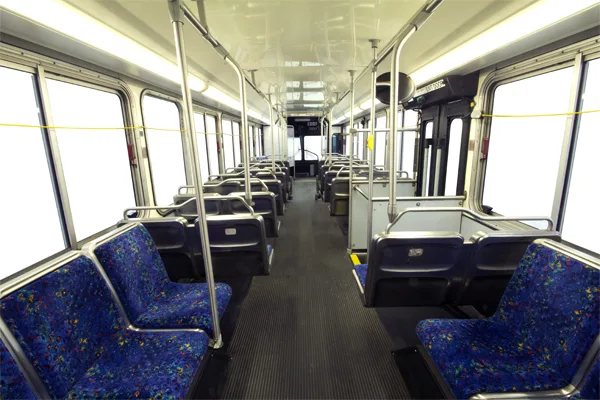 Interior of a transit-style bus with rows of blue upholstered seats, a center aisle, and large windows along both sides