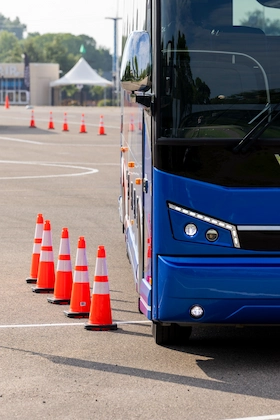 Front corner of a blue Lorenz Bus Service motorcoach navigating an orange cone driving course during UMA Expo training