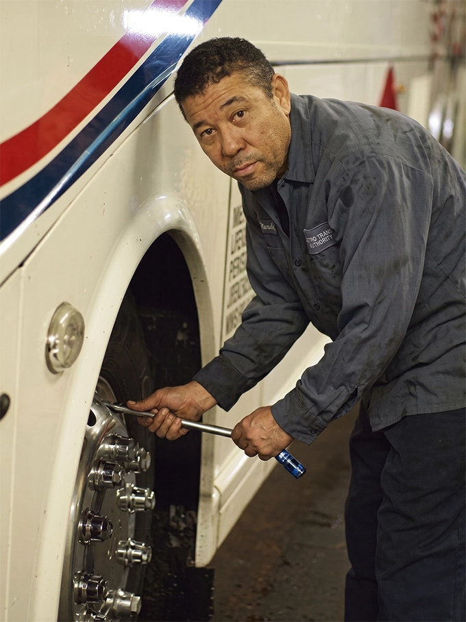 Lorenz Bus Service mechanic in uniform using a torque wrench on a motorcoach wheel in the maintenance bay