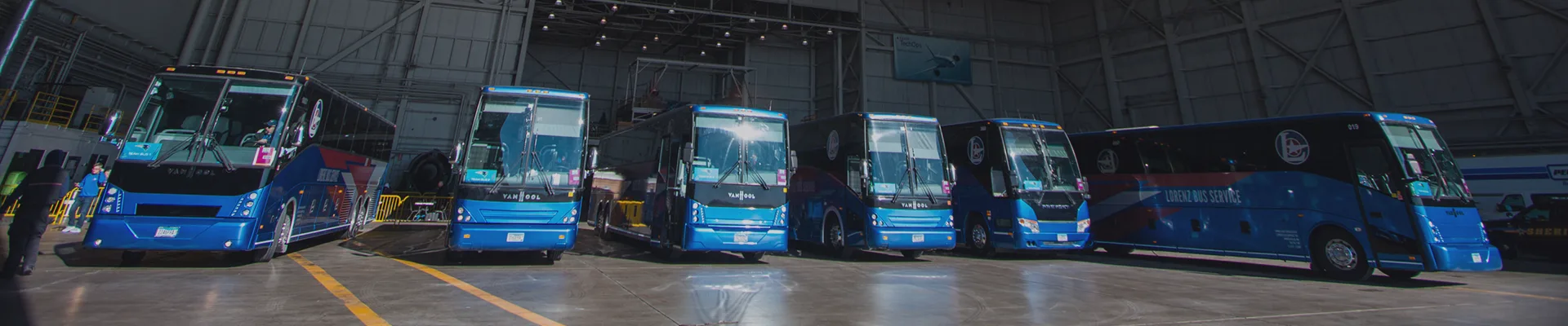 Six blue Lorenz Bus Service motorcoaches lined up inside a large industrial hangar with exposed steel trusses