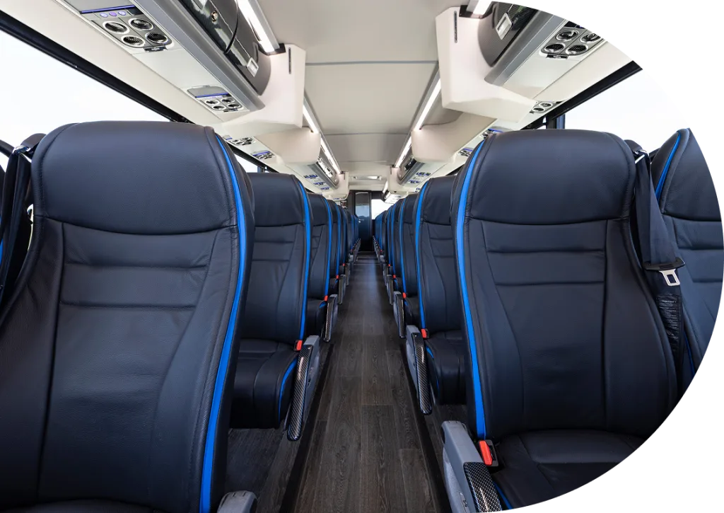 Motorcoach interior aisle view with black leather reclining seats, blue piping, seatbelts, and overhead consoles