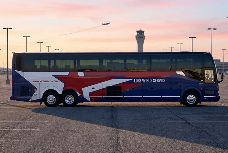 Lorenz Bus Service motorcoach parked at an airport tarmac at sunset, with an air traffic control tower in the background