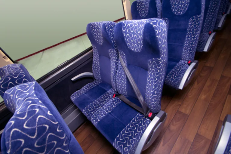 Padded blue coach bus seats with seat belts and hardwood-style flooring