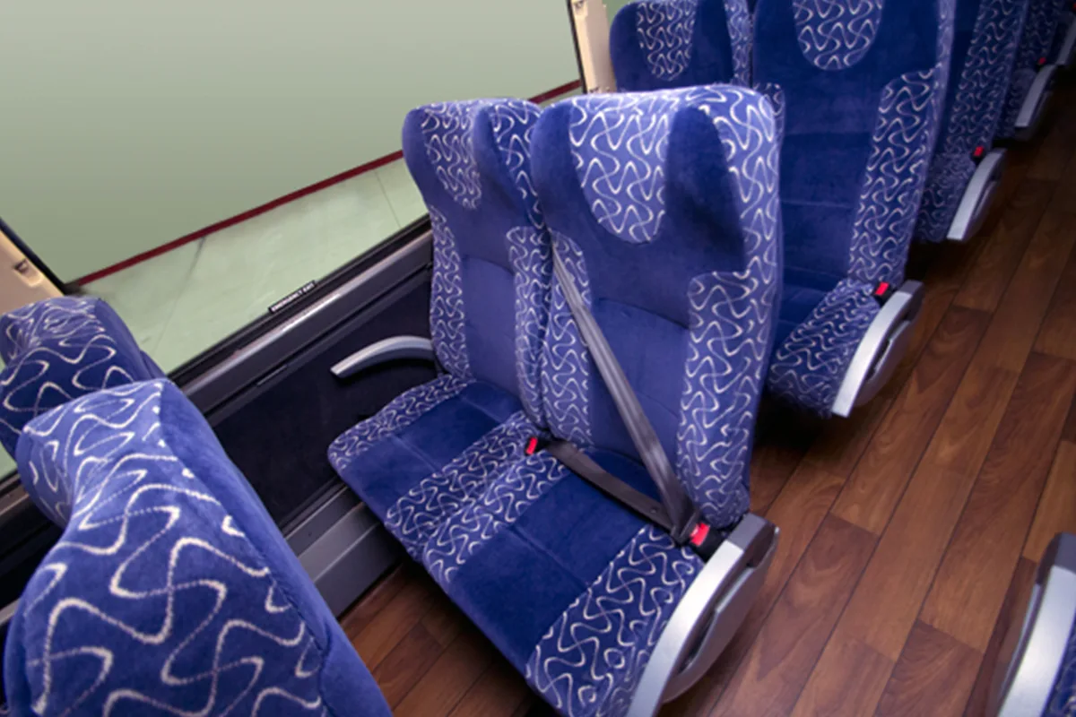 Padded blue coach bus seats with seat belts and hardwood-style flooring