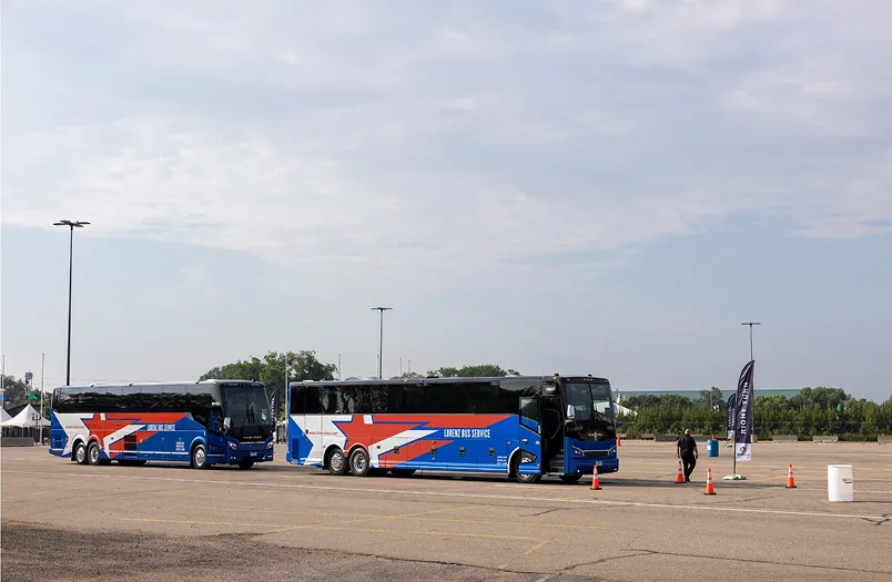 Two blue Lorenz Bus Service motorcoaches parked at an outdoor driver training course with cones and a staff member nearby