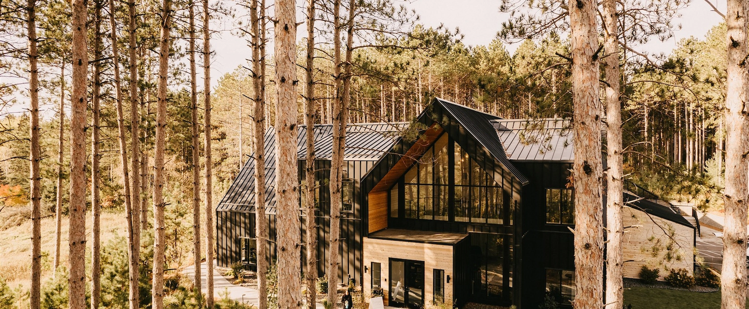 Modern black and wood event venue with floor-to-ceiling windows nestled among tall pine trees at Pinewood Weddings and Events