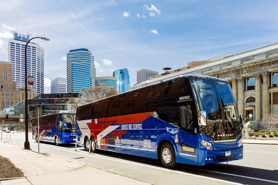 Two Lorenz Bus Service Prevost motorcoaches parked on a downtown Minneapolis street with skyscrapers and a federal building behind