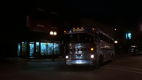 Vintage Lorenz bus driving at night on a small-town street in a screenshot from the film The Cure