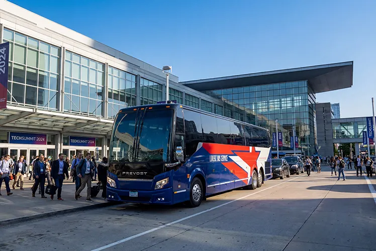 Lorenz Bus Service Prevost motorcoach parked outside a convention center during TechSummit 2024, with attendees boarding nearby