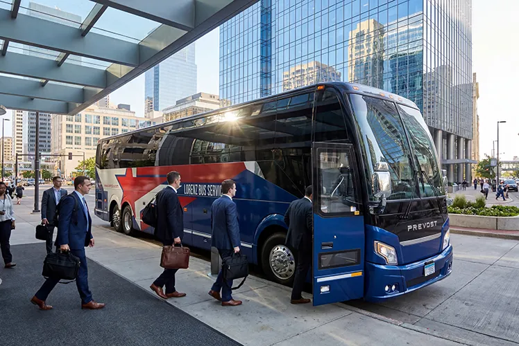 Business travelers in suits boarding a Lorenz Bus Service Prevost coach outside a downtown high-rise