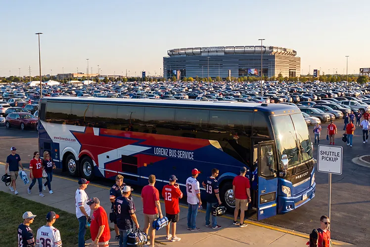 Lorenz Bus Service coach at a stadium shuttle pickup area, with fans in team jerseys boarding in a packed game-day parking lot