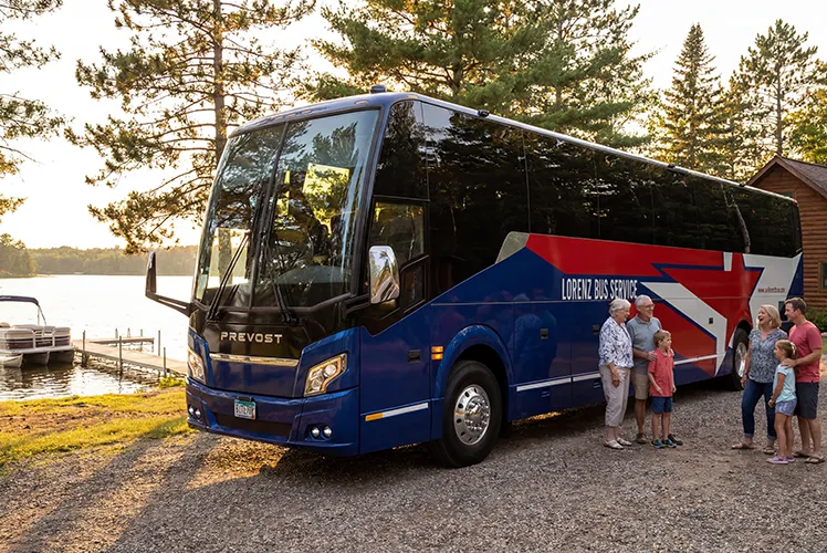A Lorenz Bus Service Prevost motorcoach parked lakeside at sunset with a multigenerational family gathered near the door