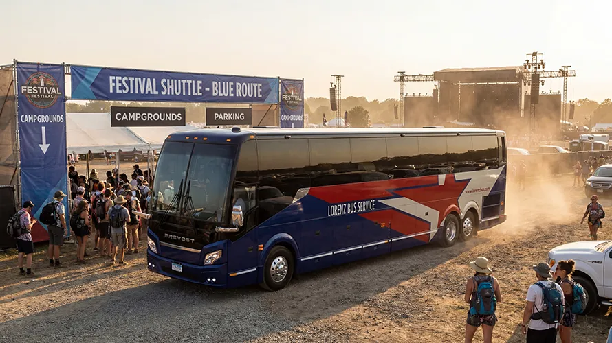Lorenz Bus Service Prevost coach operating a festival shuttle blue route with festivalgoers boarding near campgrounds and a main stage