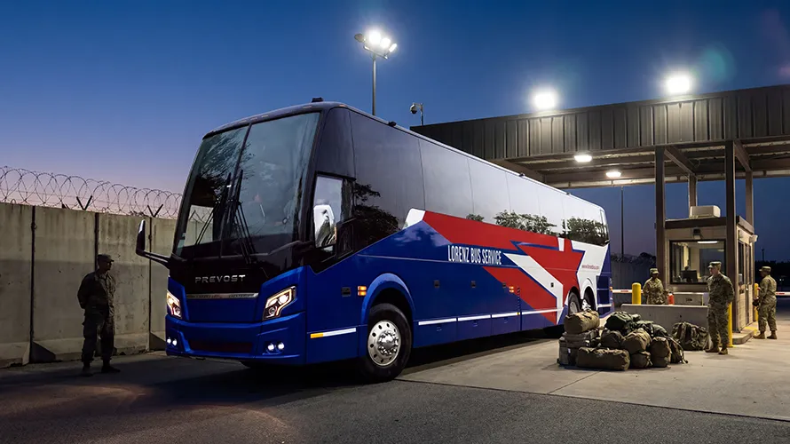 Lorenz Bus Service Prevost charter bus at a military base checkpoint at night, with soldiers and gear staged nearby