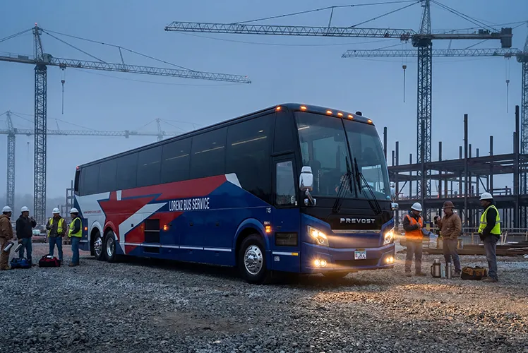 Lorenz Bus Service motorcoach parked at an active construction site at dusk, with crew members in hard hats and safety vests boarding nearby