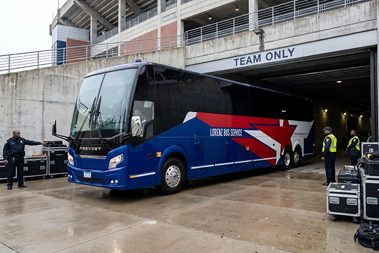 Lorenz Bus Service Prevost coach entering a stadium's Team Only tunnel, with security staff and equipment cases nearby