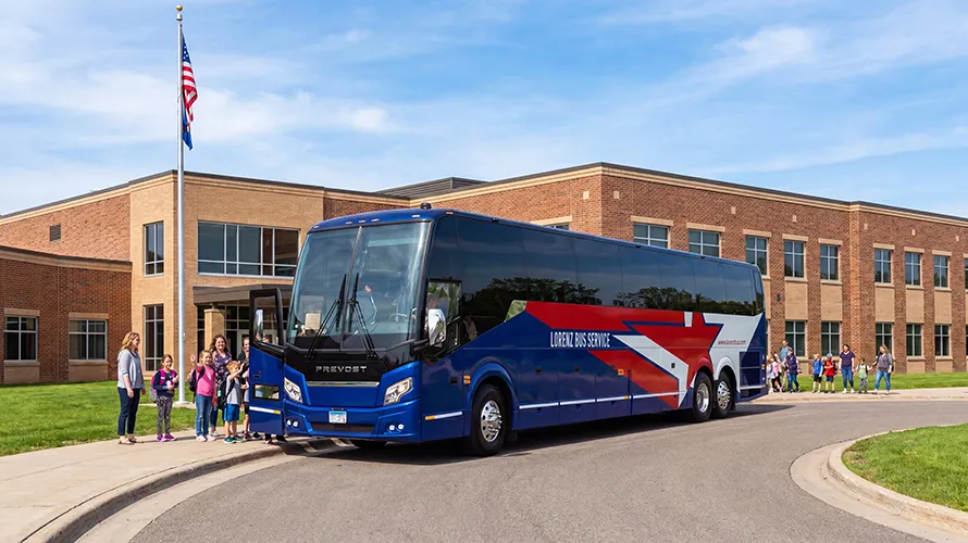 Lorenz Bus Service Prevost motorcoach parked in front of a school as students and a teacher gather to board