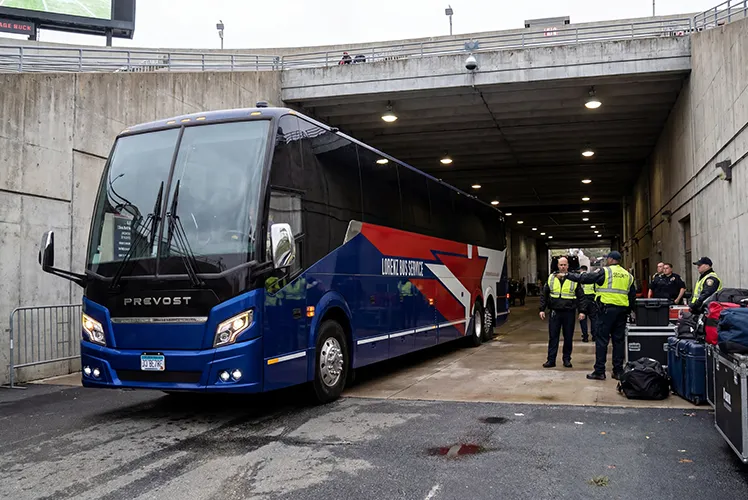 Lorenz Bus Service Prevost charter coach entering a stadium tunnel, with security personnel and equipment cases nearby