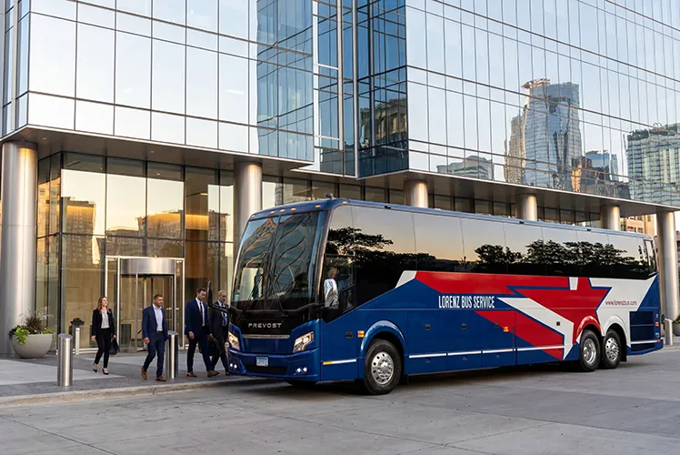 Lorenz Bus Service Prevost motorcoach parked outside a glass office building as professionally dressed passengers board