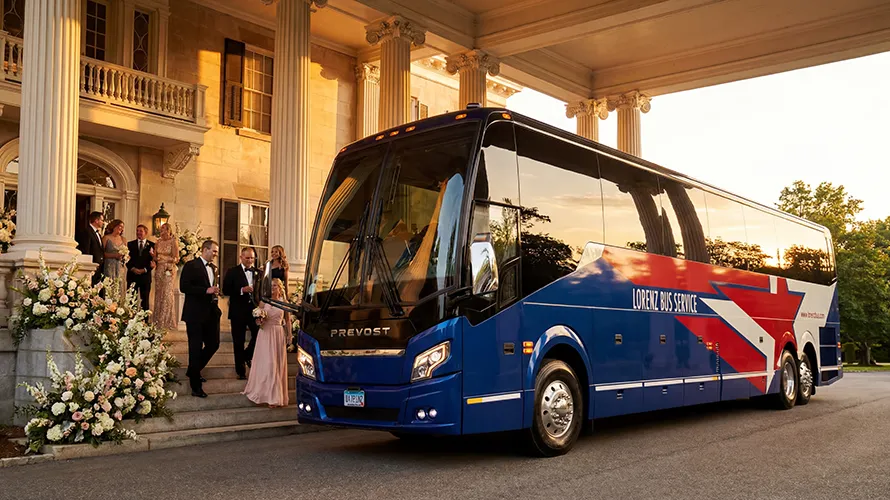 Lorenz Bus Service motorcoach parked outside a wedding venue as formally dressed guests gather on the steps at sunset