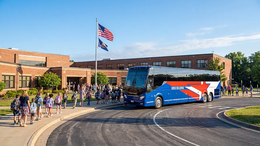 Students with backpacks boarding a Lorenz Bus Service Prevost motorcoach in front of a brick school building