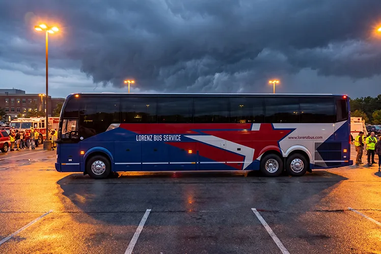 Lorenz Bus Service motorcoach parked in a lot at dusk, with staff in safety vests visible on both sides