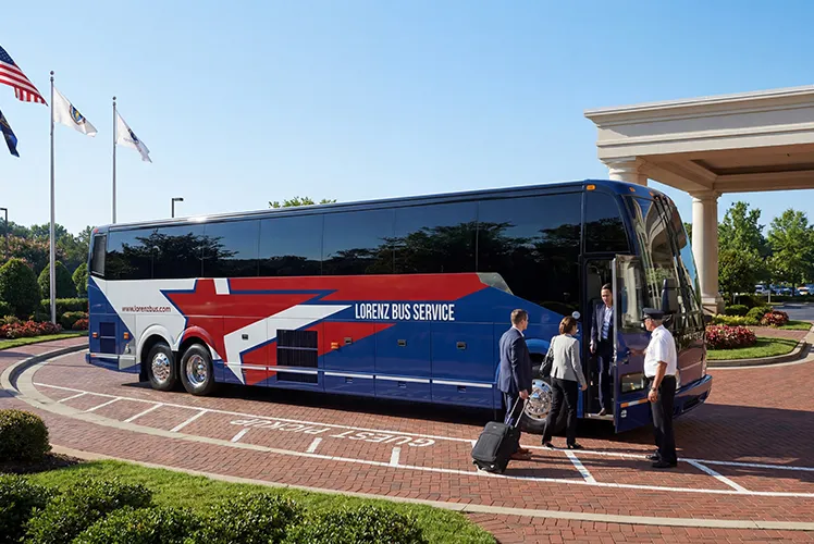 Lorenz Bus Service motorcoach parked at a hotel entrance as a uniformed driver greets boarding passengers with luggage
