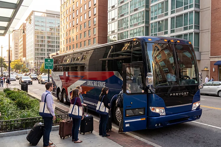 Passengers with luggage boarding a Lorenz Bus Service Prevost motorcoach at a downtown shuttle pickup stop