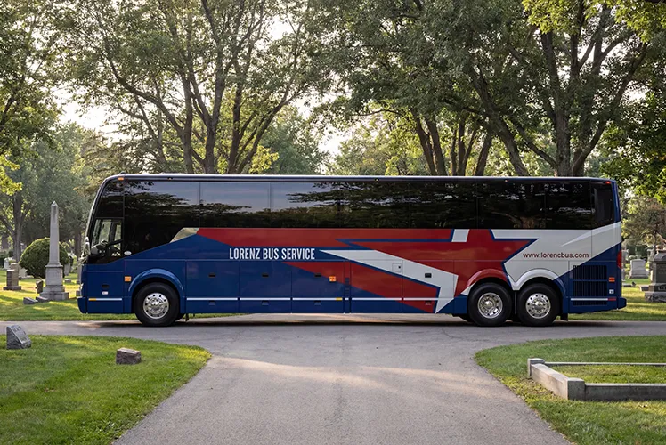 Lorenz Bus Service full-size motorcoach with blue, red, and white livery parked on a tree-lined drive