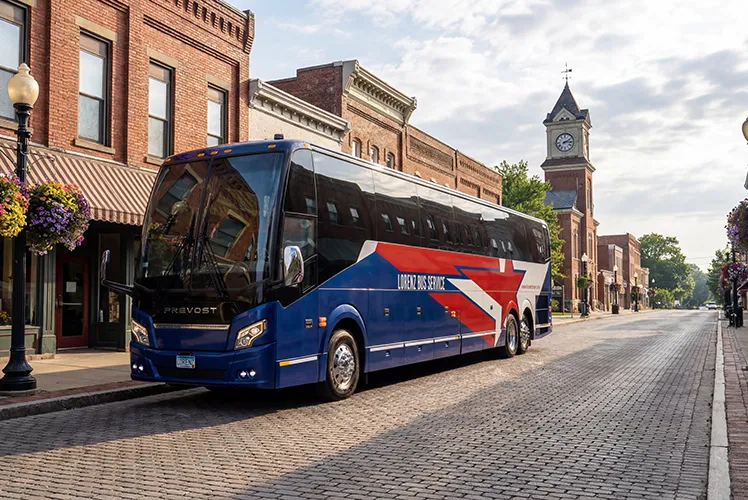 Lorenz Bus Service Prevost motorcoach on a brick-paved small-town street lined with historic storefronts and a clock tower
