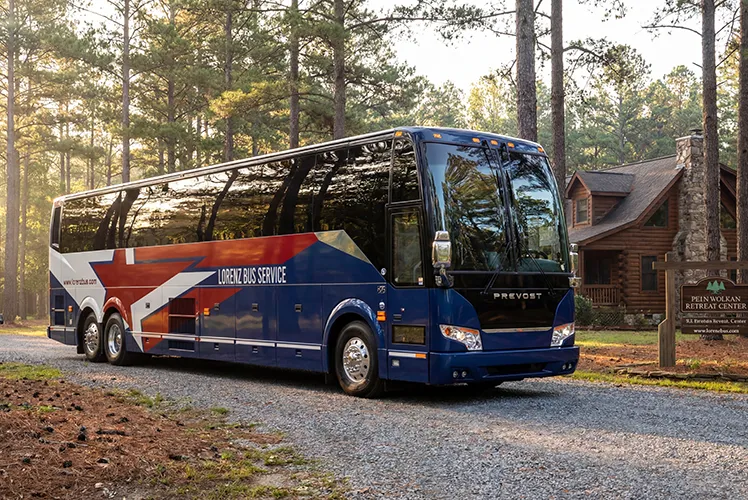 Lorenz Bus Service Prevost motorcoach parked at a wooded retreat center, surrounded by tall pines at golden hour