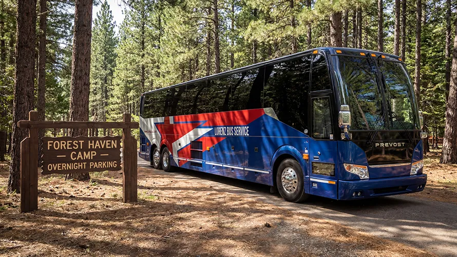 Lorenz Bus Service Prevost charter coach parked at Forest Haven Camp overnight parking area among tall pine trees