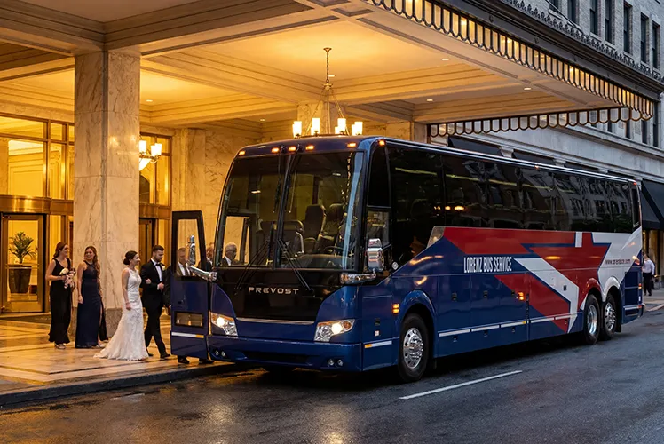A bride, groom, and wedding party boarding a Lorenz Bus Service motorcoach outside a hotel entrance at night